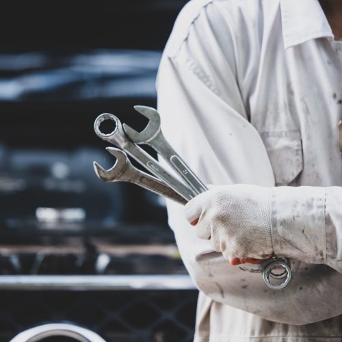 Car repairman wearing a white uniform standing and holding a wrench that is an essential tool for a mechanic